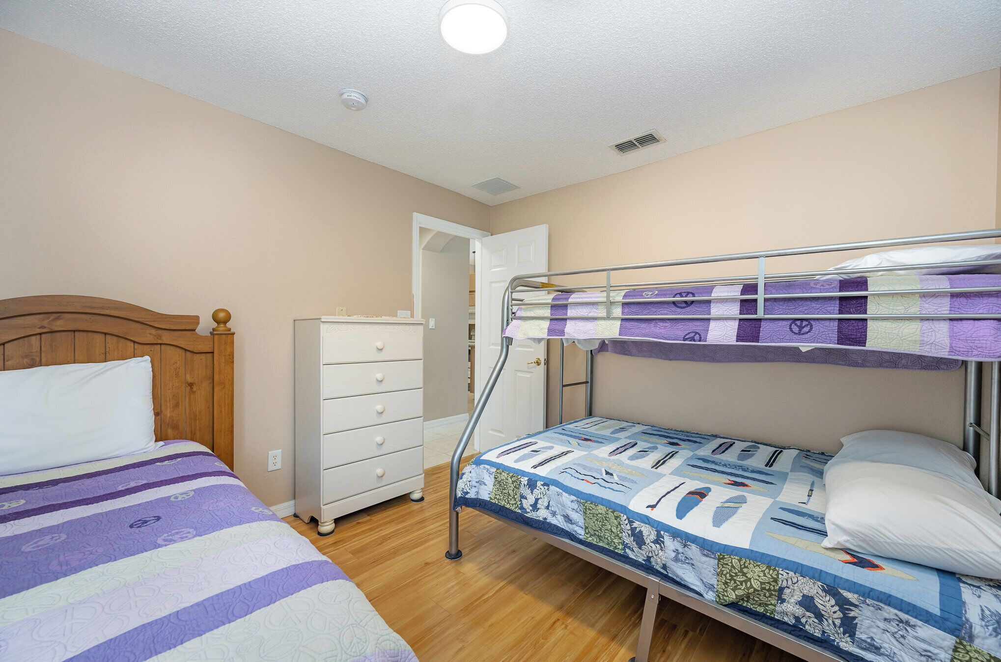 Een slaapkamer met een stapelbed, een enkel bed, een dressoir en een deur naar een andere kamer.