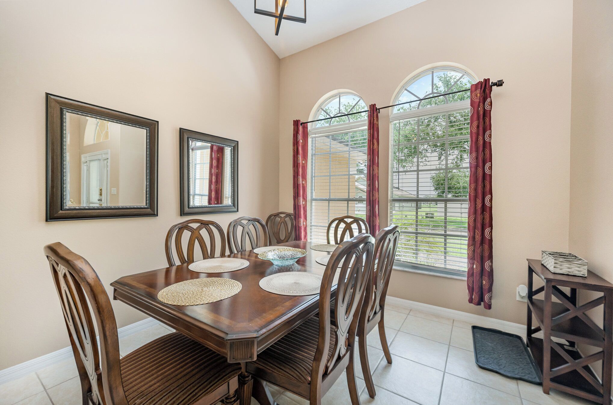 A dining area with a wooden table, six chairs, two wall mirrors, and a window with curtains.