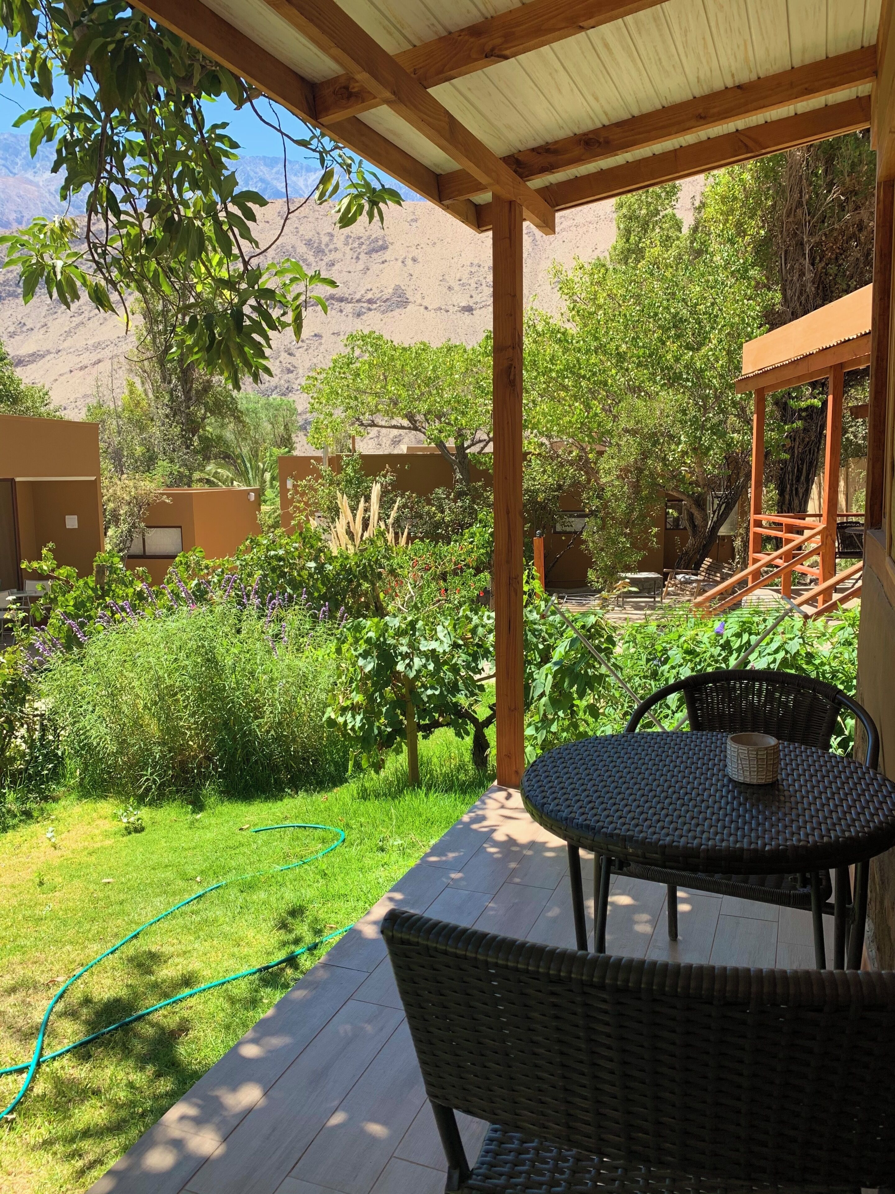 Une terrasse couverte avec une table et des chaises, entourée de verdure et offrant une vue sur les montagnes.