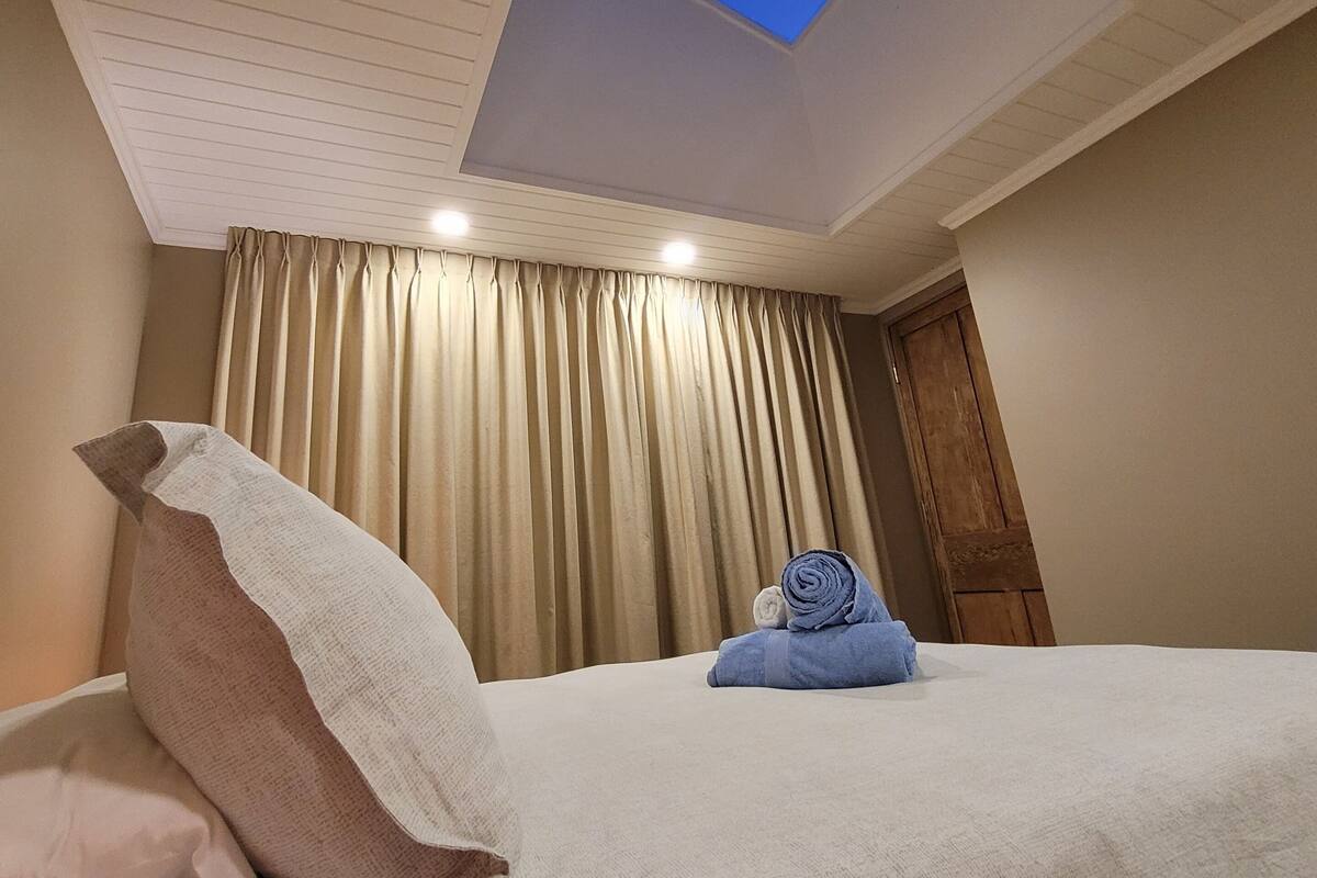 Habitación de hotel con tragaluz, una cama con una toalla enrollada y un ventanal con cortinas.