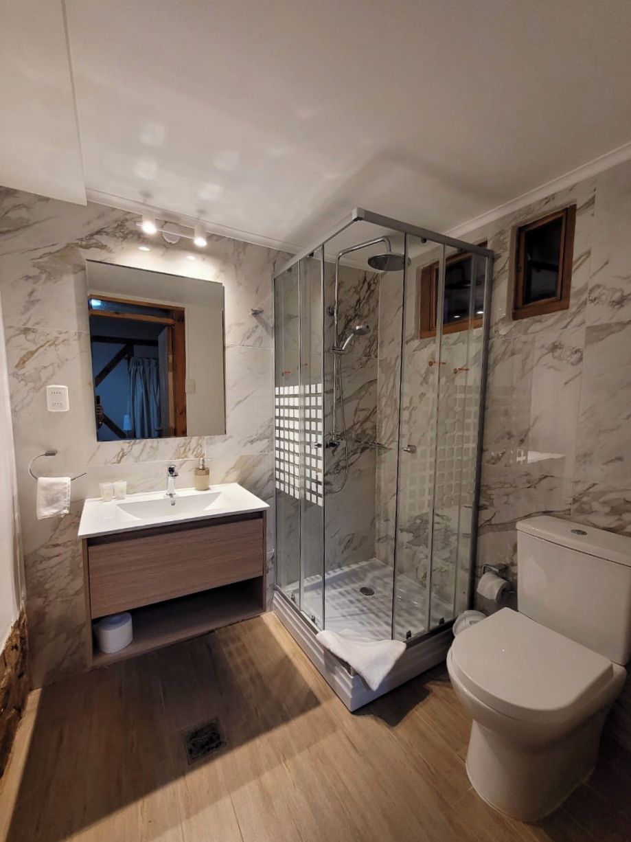 A bathroom with a glass-enclosed shower, a white sink with a marble countertop, and a toilet.