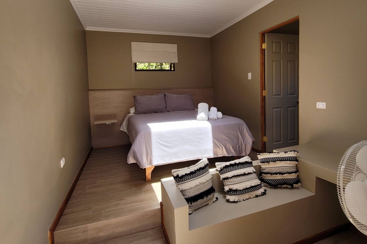 Un dormitorio con tragaluz, una cama, una mesita de noche con toallas, un ventilador y una escalera.