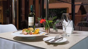 Mesa lista para comer con una botella de vino, una copa y un plato de comida, con vista a la montaña al fondo.