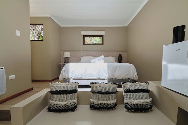 A bedroom with a bed, bedside lamp, window, and a white appliance on the wall. - El Tesoro de Elqui (Paiguano)