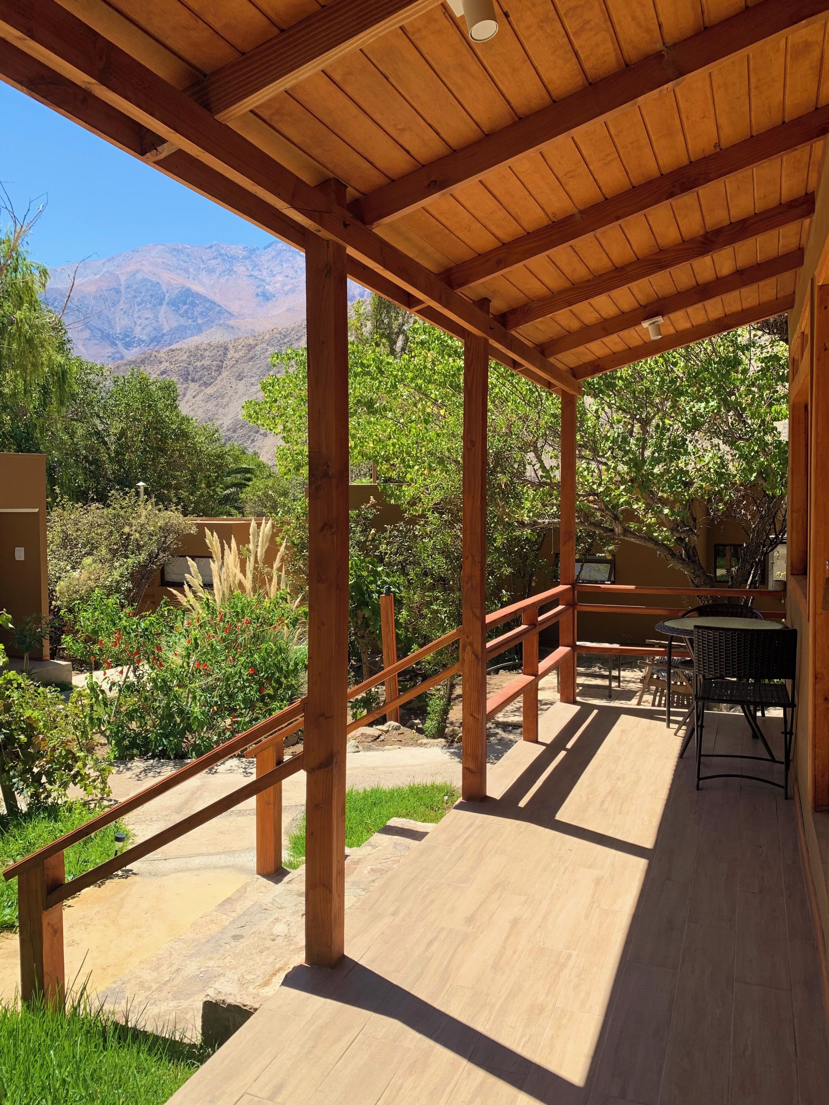 A covered outdoor area with wooden beams, a table with chairs, and a view of mountains.