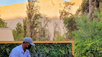 Dos personas sentadas al aire libre, con un fondo de vegetación y un paisaje montañoso.