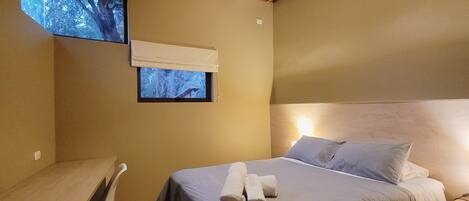 A bedroom with a bed, a desk, and a window with a view of trees.