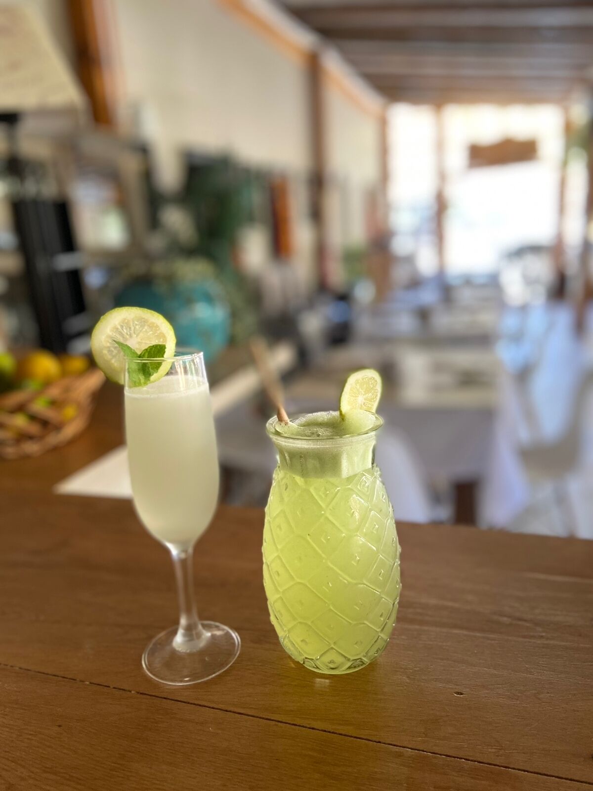 Two drinks on a wooden table, one in a clear glass and the other in a textured glass, both garnished with a lime slice.