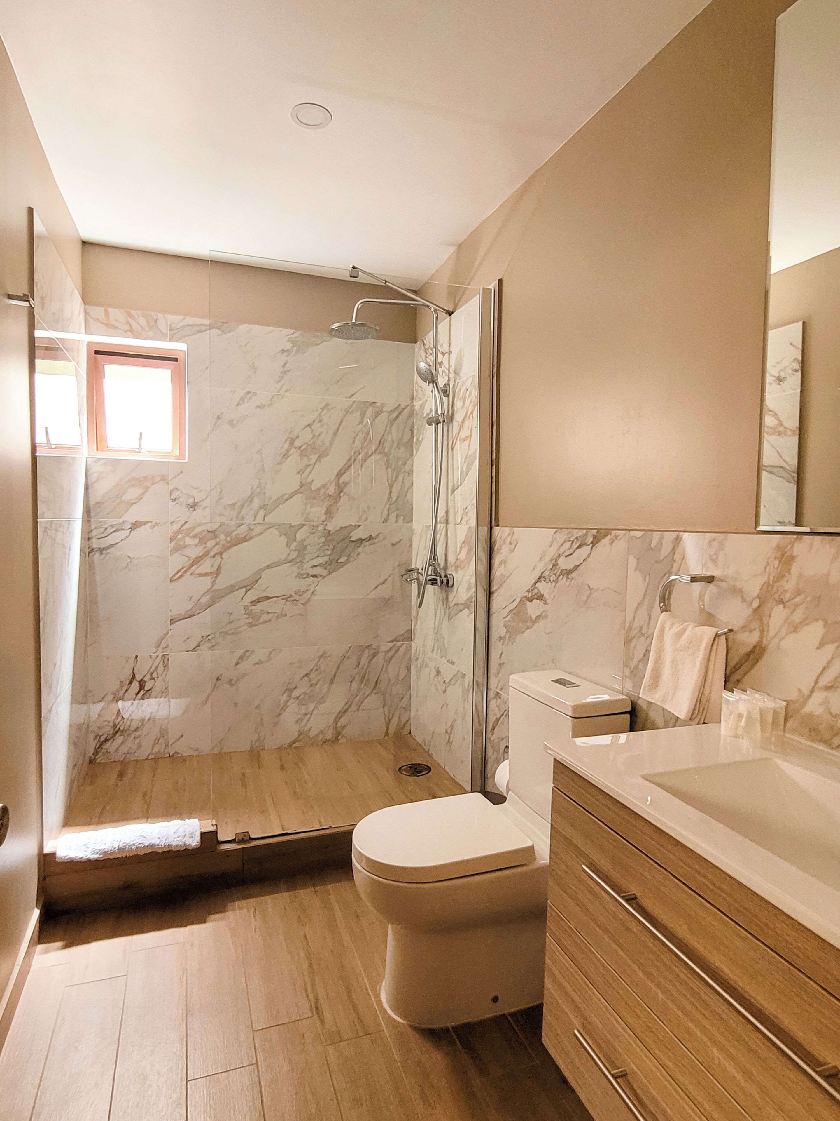 A bathroom with a shower, toilet, vanity, and marble walls.