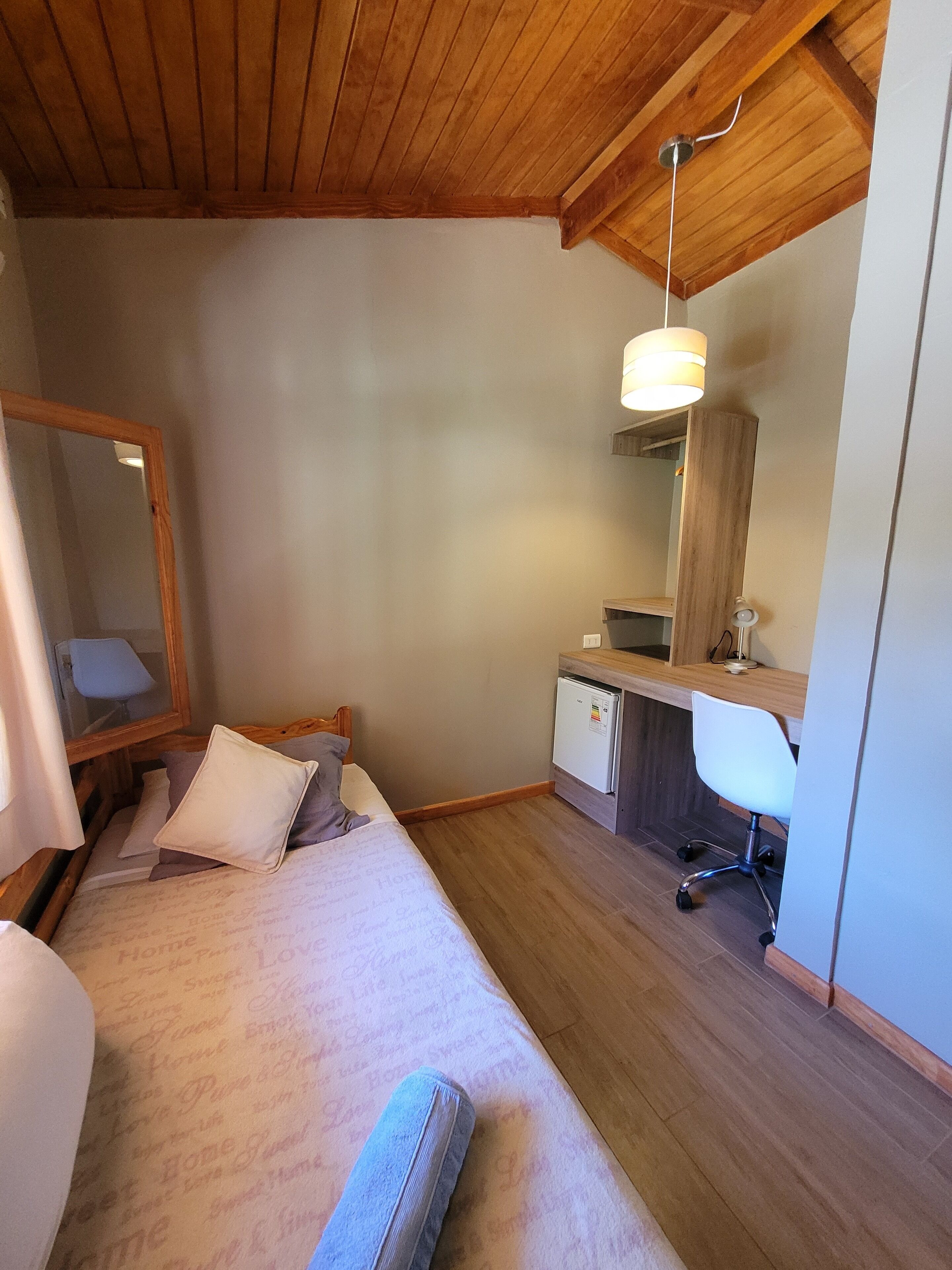 A bedroom with a bed, a desk, a chair, a mirror, and a ceiling light fixture.