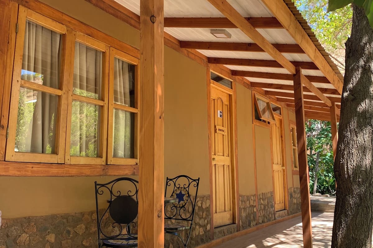 Un edificio de madera con un porche cubierto, paredes de piedra y una silla de metal.