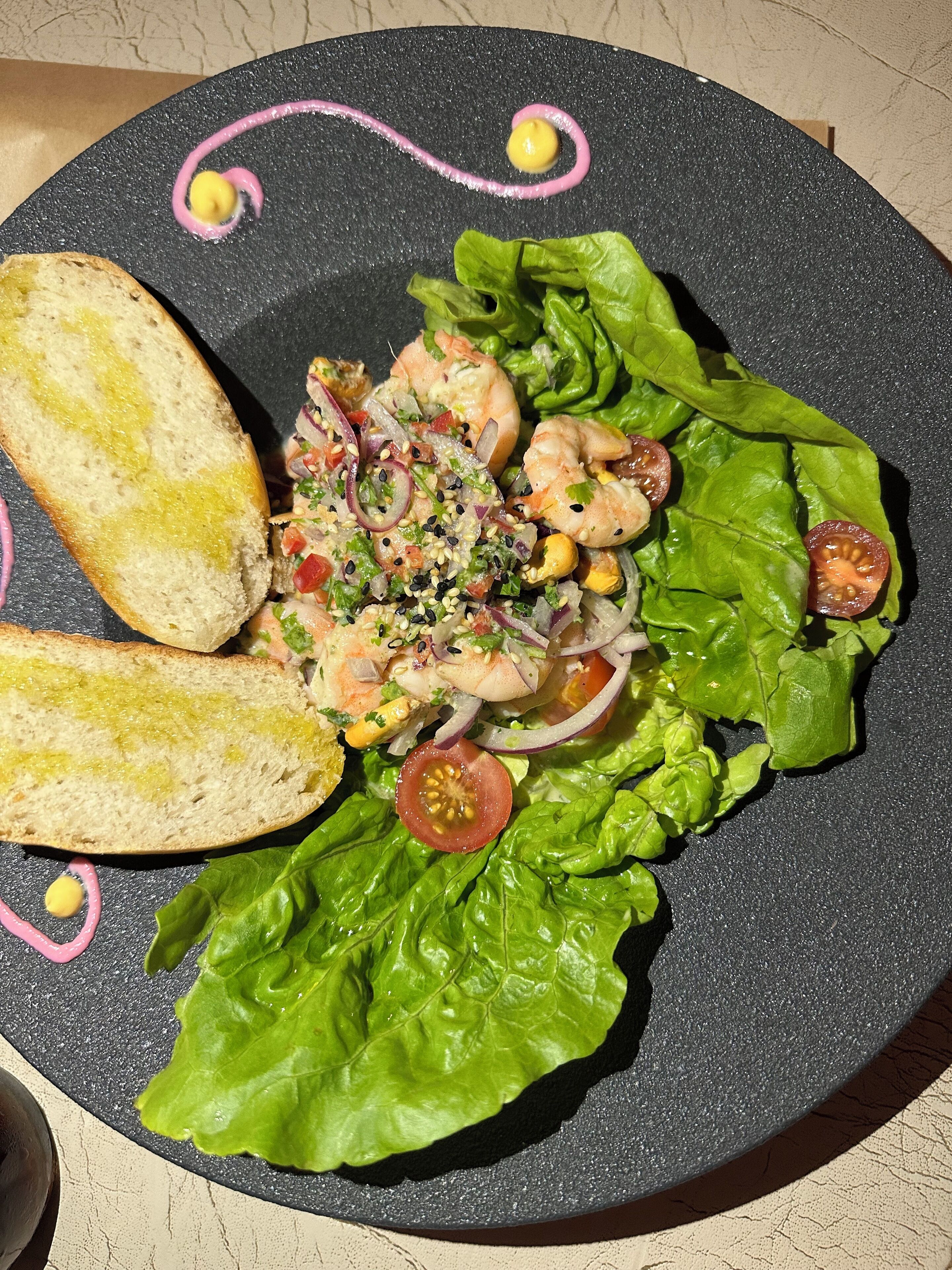 Ein Teller Garnelensalat mit Salat und Tomaten, dazu geröstetes Brot.
