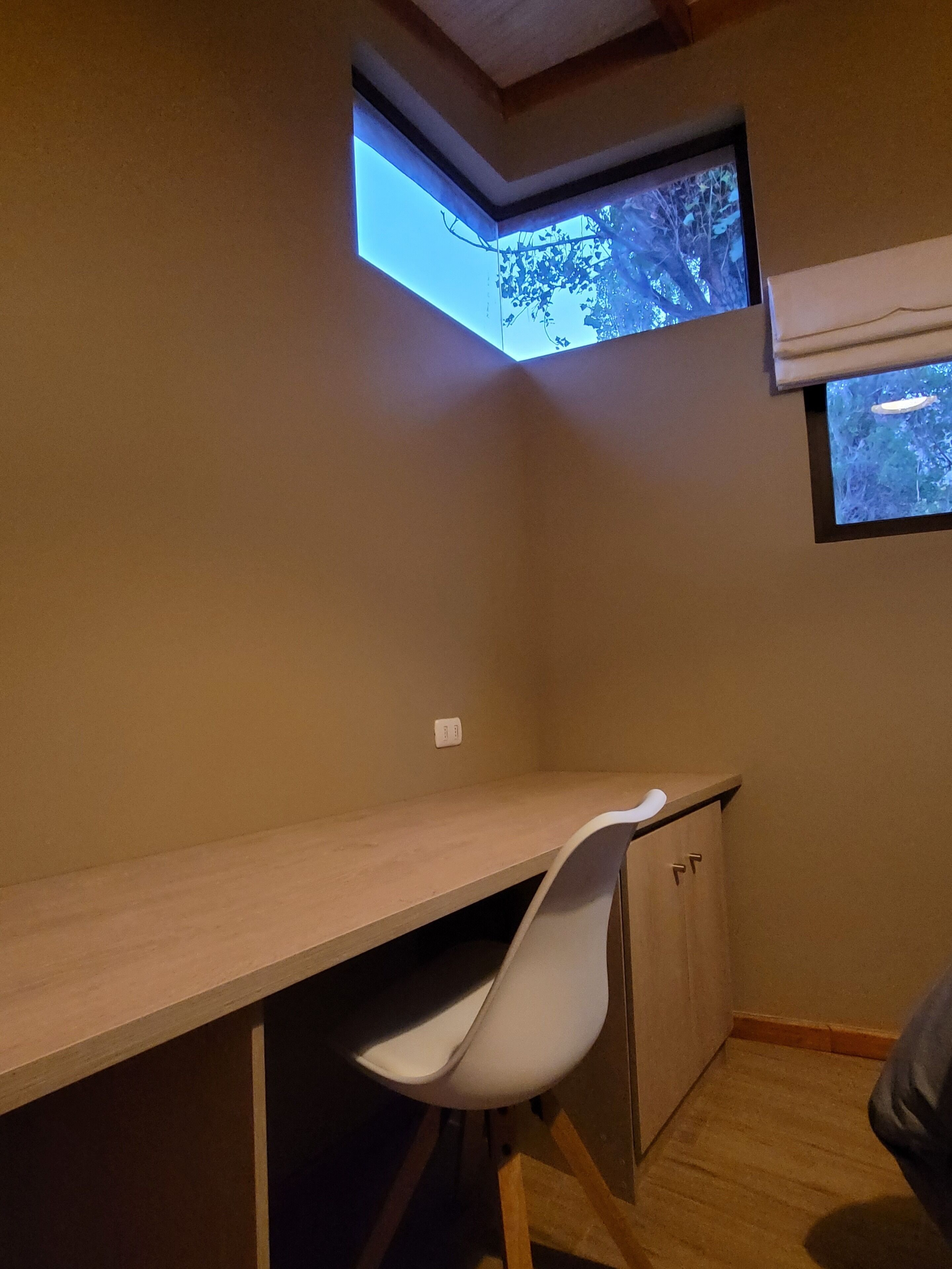 A corner room with a desk, chair, and a small window.