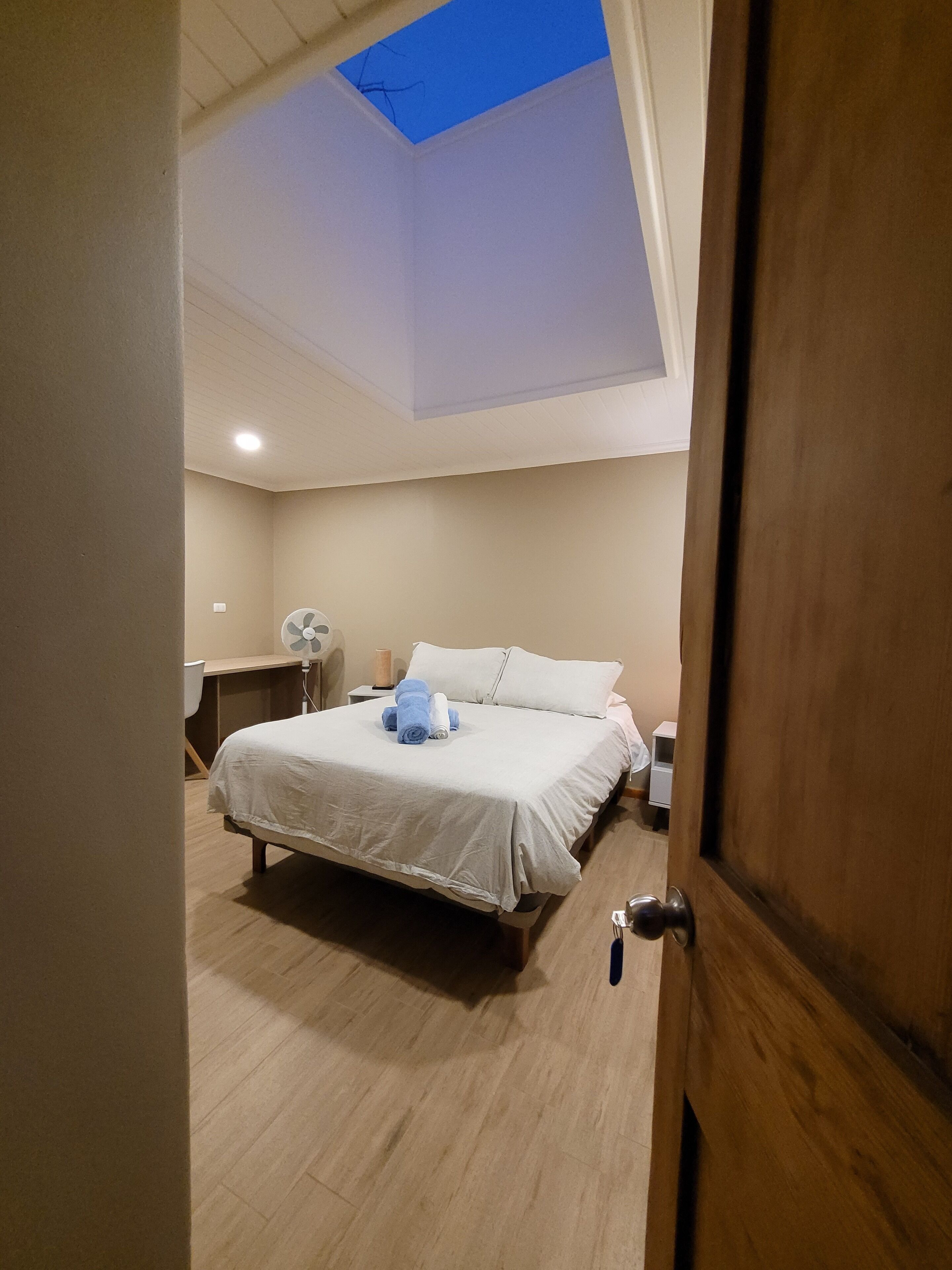 Un dormitorio con una cama, un escritorio, una silla, un ventilador y una lámpara de techo.