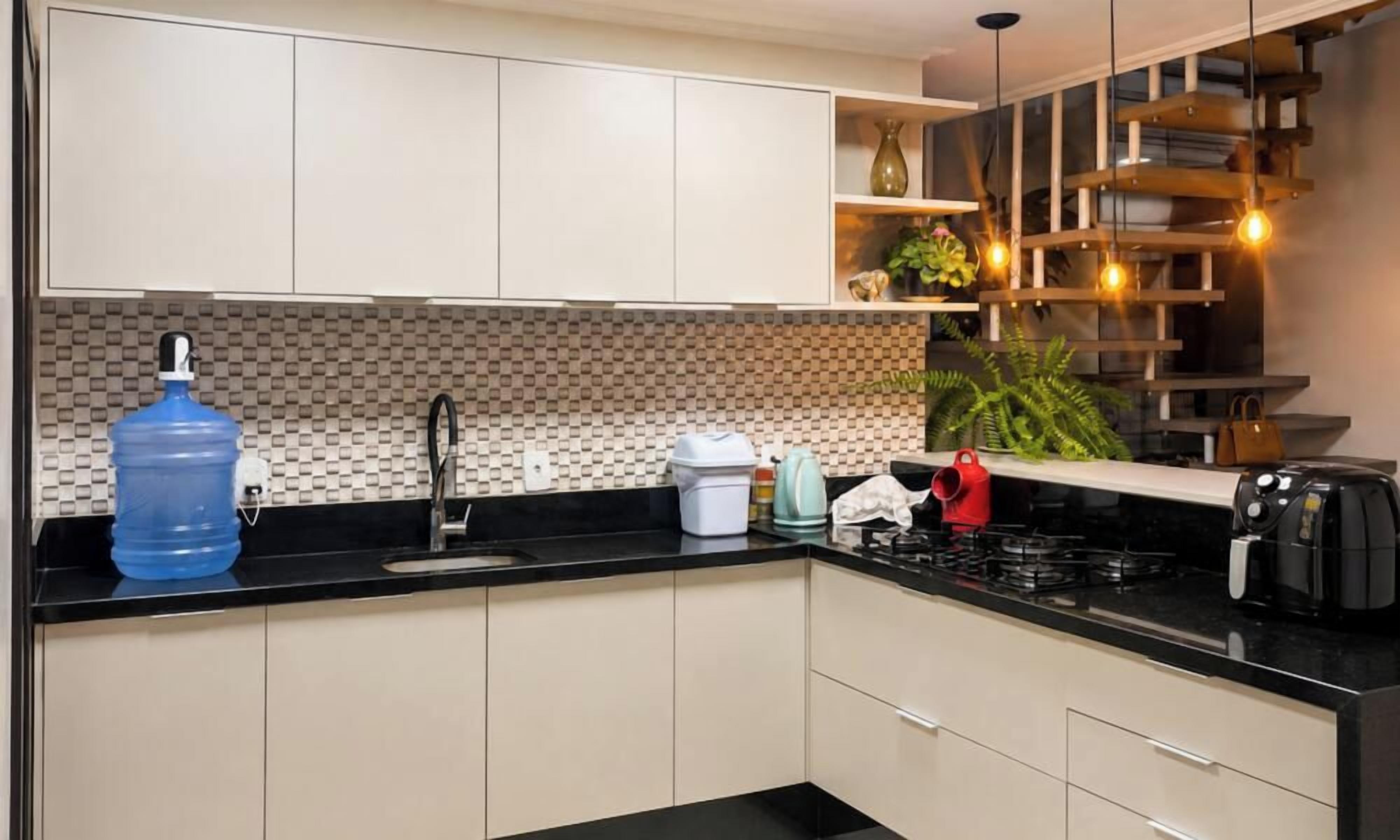 A modern kitchen with a black countertop, a large water dispenser, a coffee maker, and a red kettle.