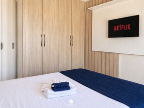 A hotel room with a bed, a wall-mounted television displaying 'NETFLIX', and a wooden wardrobe. - Casa Comfort Rio Vermelho - Florianópolis (Florianópolis)