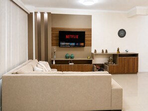 A modern living room with a beige sofa, a wooden entertainment unit, and a flat-screen TV displaying the Netflix logo. - Casa Comfort Rio Vermelho - Florianópolis (Florianópolis)