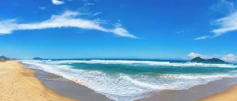 A beach with waves, a clear sky, and distant mountains.