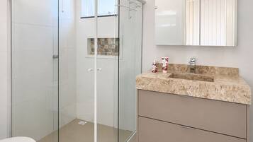 A modern bathroom with a glass-enclosed shower, a beige marble countertop, and a large mirror above the sink.