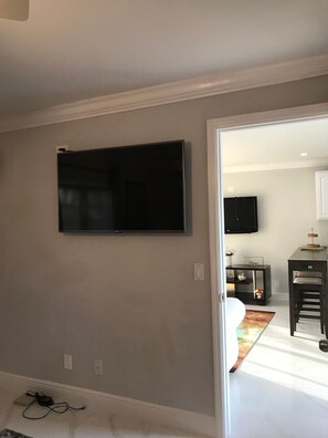 A room with a mounted TV, a small table with a sign, and a door leading to another room. - The Havens Hideaway (Freeport)