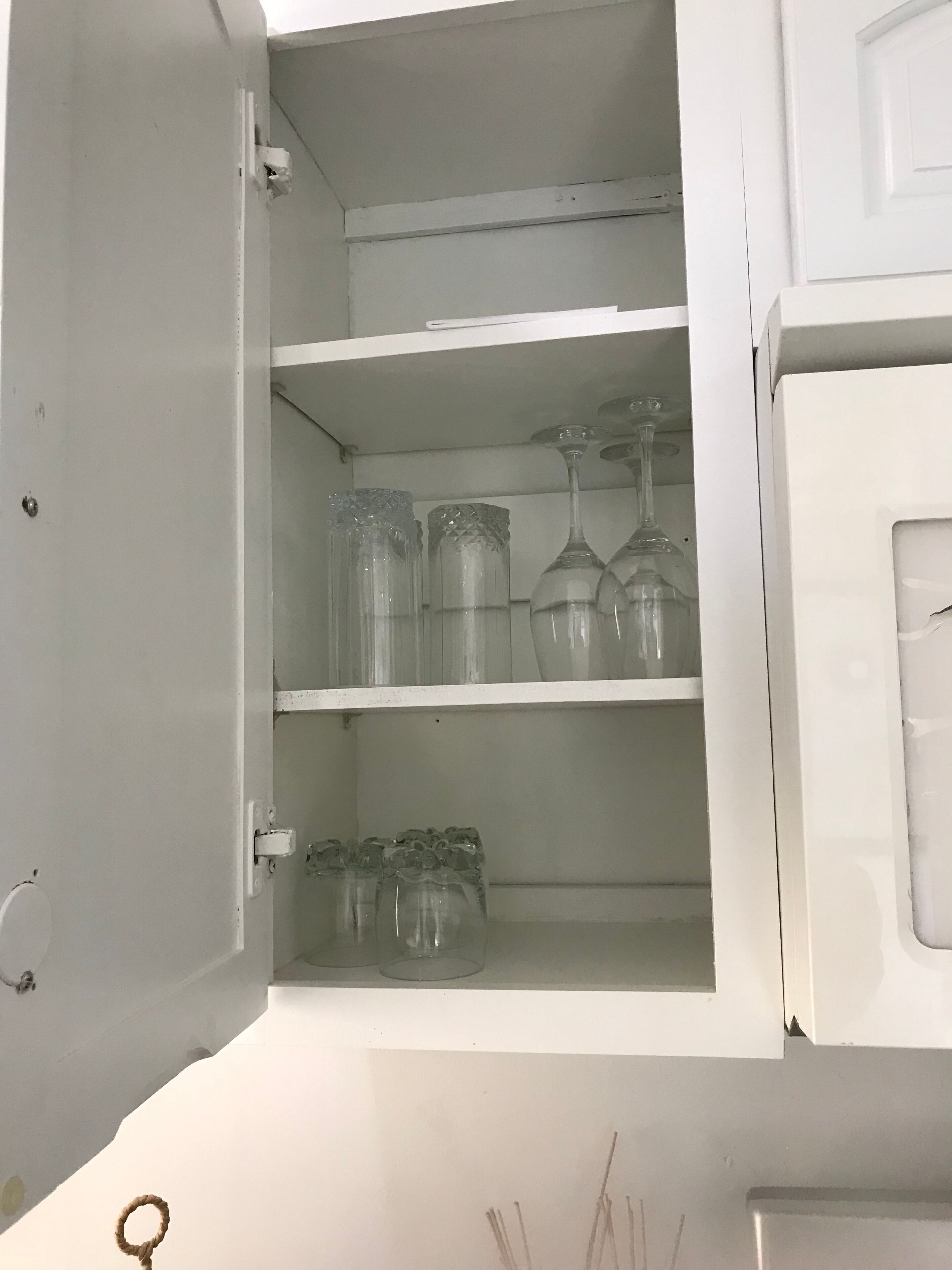 An open cabinet with shelves containing clear glassware and a white door.