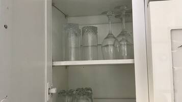An open cabinet with shelves containing clear glassware and a white door.