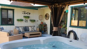 Um pátio externo acolhedor com hidromassagem, móveis de vime e plantas em vasos.