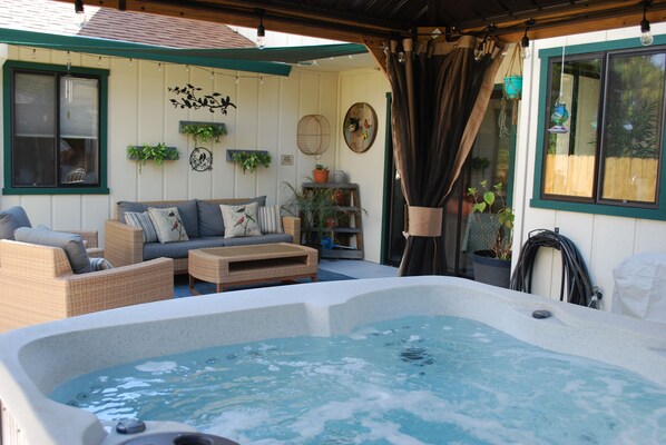 A cozy outdoor patio with a hot tub, wicker furniture, and potted plants. - Sweet & Cozy, Bird Themed Nest, w/ Hot Tub & Fire Pit. 9 min to Turtle Bay (Redding)