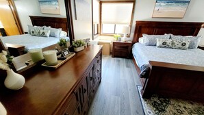 Quarto de hotel com duas camas, cômoda de madeira, espelho e janela com vista para a praia.