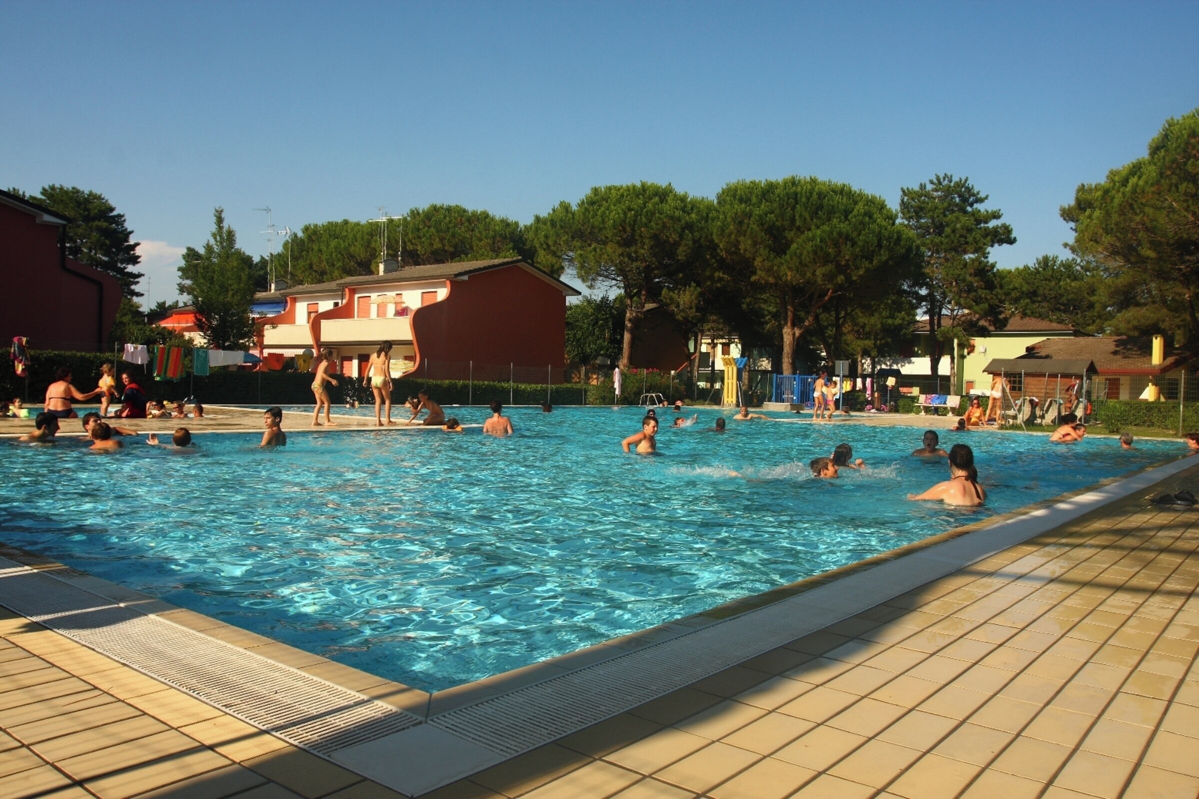 A swimming pool with people in it, surrounded by buildings and trees.