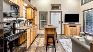 Une cuisine de taille réduite, dotée de meubles en bois, d’un four à micro-ondes, d’une cuisinière et d’un téléviseur.