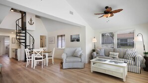 Un vaste espace de vie comprenant un escalier, des canapés à rayures, une table basse et un ventilateur de plafond.