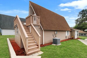 Una casa de dos pisos con una escalera de madera, un porche cubierto y un jardín con mantillo rojo.