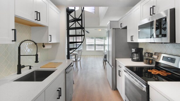 Une cuisine moderne avec des meubles blancs, un escalier en colimaçon noir et un réfrigérateur en acier inoxydable.
