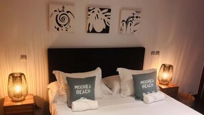A neatly made bed with two pillows labeled "MOOREA BEACH," a headboard, and three wall art pieces. - Tipanie- Apt F2 PPT w/pool, A/C, high speed Wifi and wonderful view (Papeete)