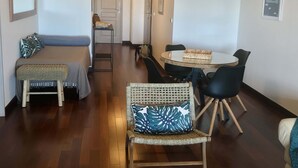 A modern living room with a sofa, a dining table with chairs, and a small round table with a chair. There are hanging lights above the dining table. - Tipanie- Apt F2 PPT w/pool, A/C, high speed Wifi and wonderful view (Papeete)