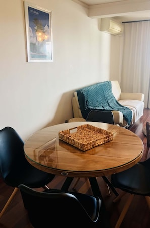 A dining area with a round glass table, black chairs, a woven tray, a teal blanket on a couch, and a poster on the wall.