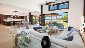 A spacious living area with a glass coffee table, a sofa, and a dining area with chairs. - Unmatched location Four Seasons Hualalai  5BR/5BA Ocean Estate 6500sqft 3/4 acre (Kailua-Kona)