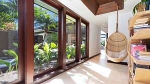 A modern interior with large windows, a hanging chair, and a bookshelf. - Unmatched location Four Seasons Hualalai  5BR/5BA Ocean Estate 6500sqft 3/4 acre (Kailua-Kona)