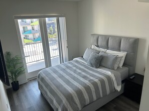 A bedroom with a bed, a nightstand, a potted plant, and a sliding glass door leading to an outdoor balcony.