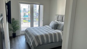 A bedroom with a bed, a potted plant, and a sliding glass door leading to an outdoor area. - Spacious & Modern 1BedRM in Noho (Burbank)