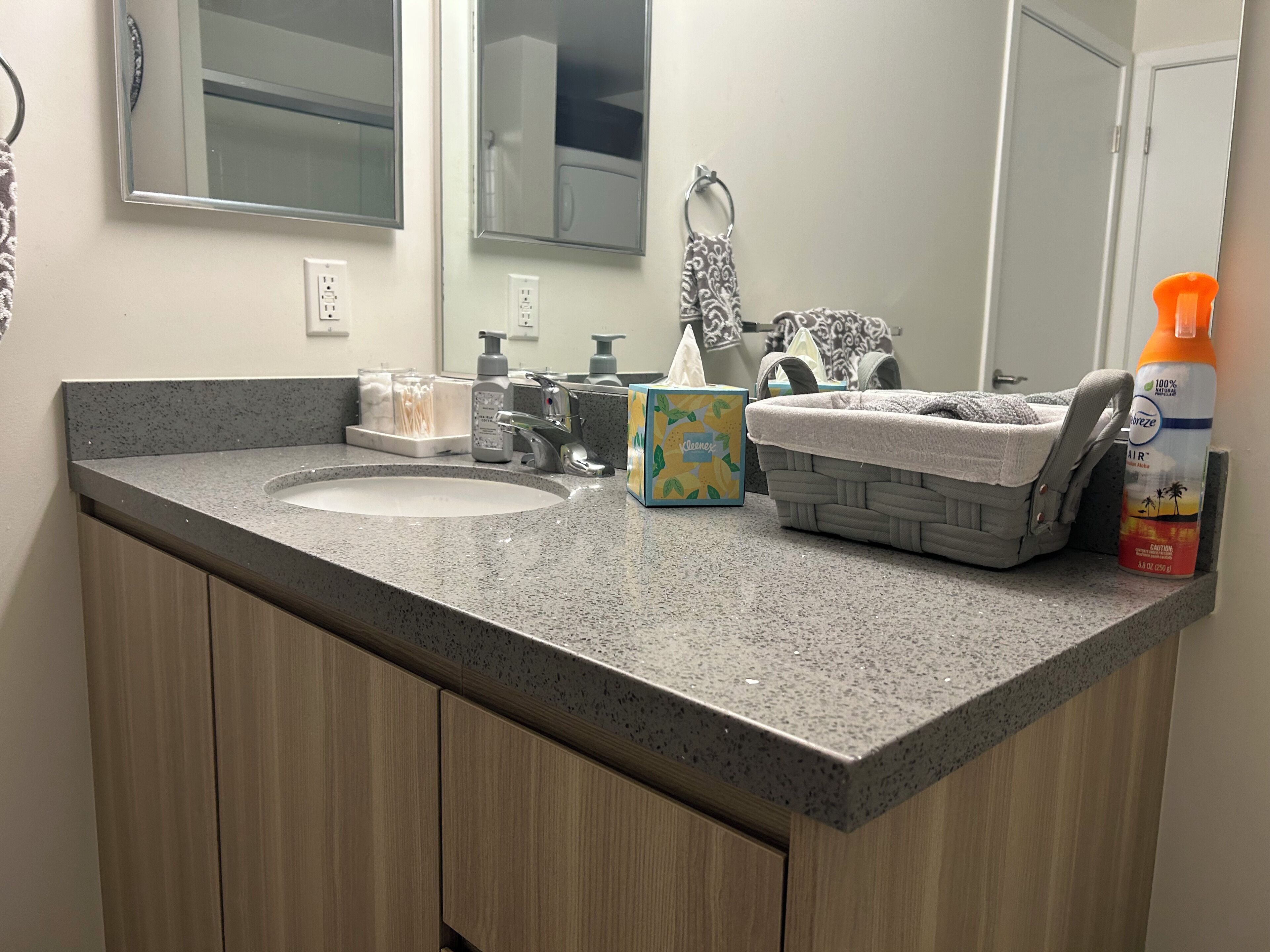 A bathroom with a granite countertop, two sinks, a mirror, a towel rack, and a basket.
