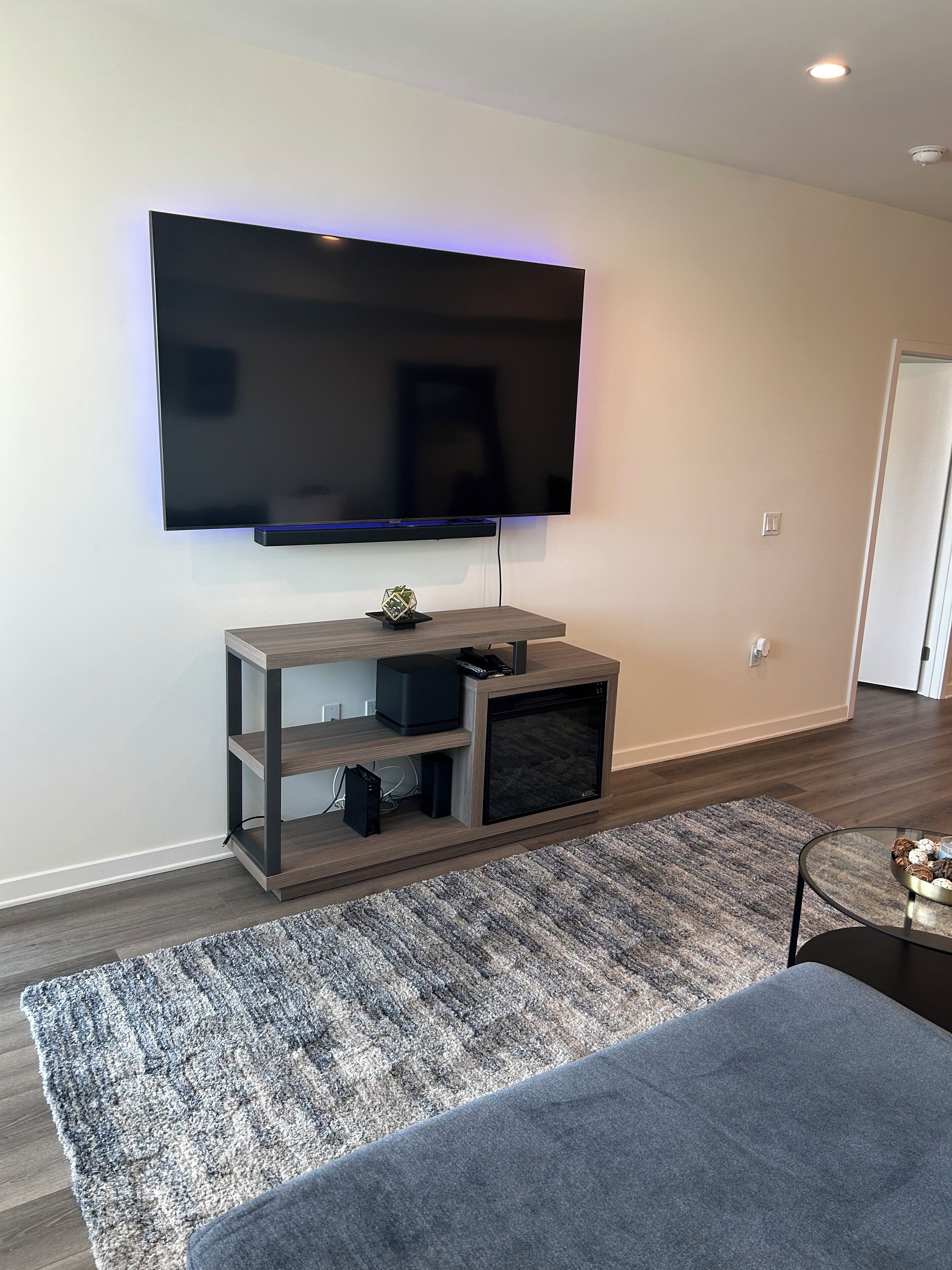 Un soggiorno moderno con una grande TV a schermo piatto montata a parete, un mobile basso in legno sottostante e un tappeto grigio sul pavimento.