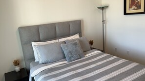 A neatly made bed with a striped bedspread, a grey upholstered headboard, and two bedside tables with decorative items.