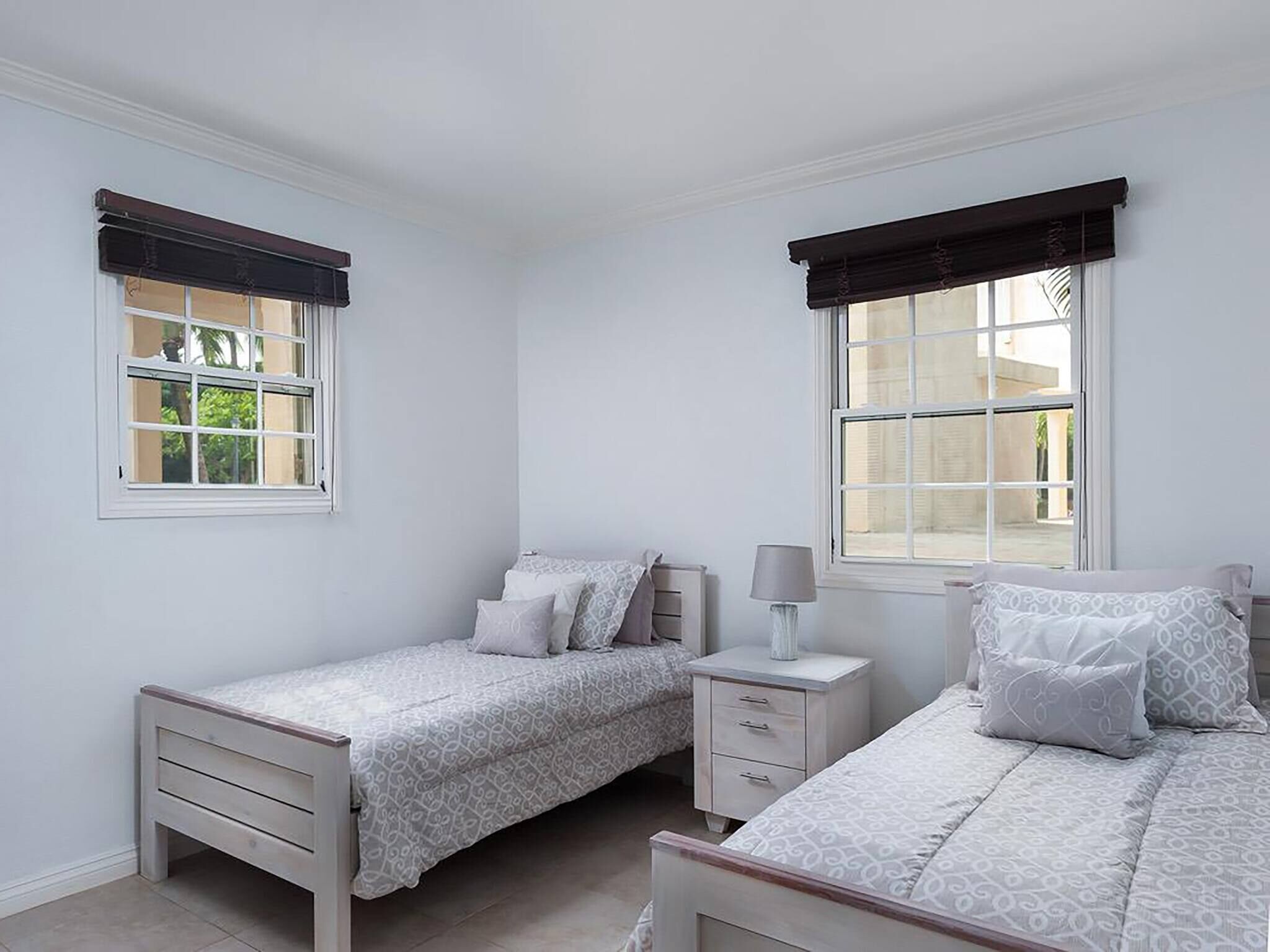 Un dormitorio con dos camas individuales, una mesita de noche con lámpara y una ventana con cortina oscura.