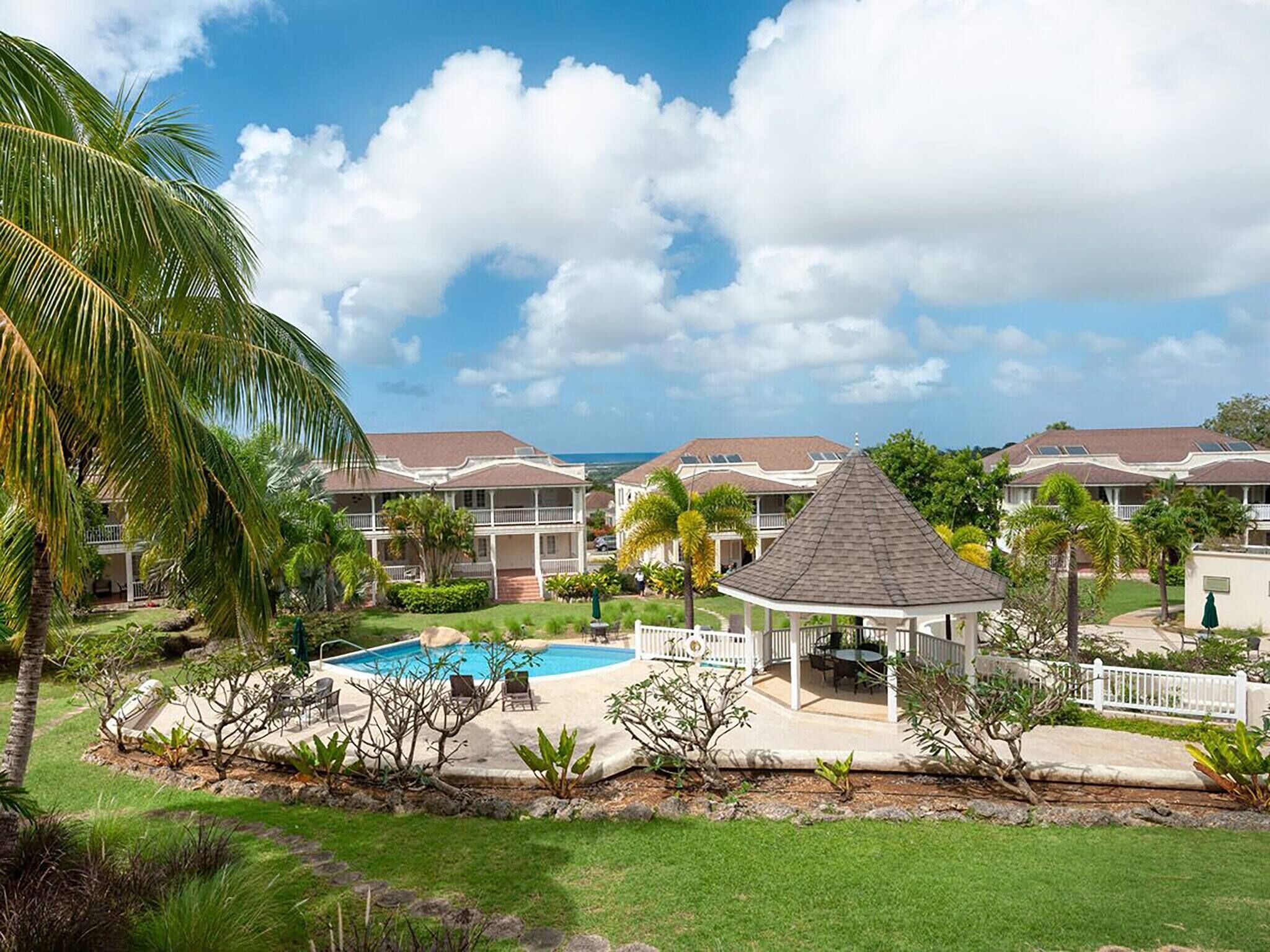 A resort with a pool, palm trees, and a gazebo.