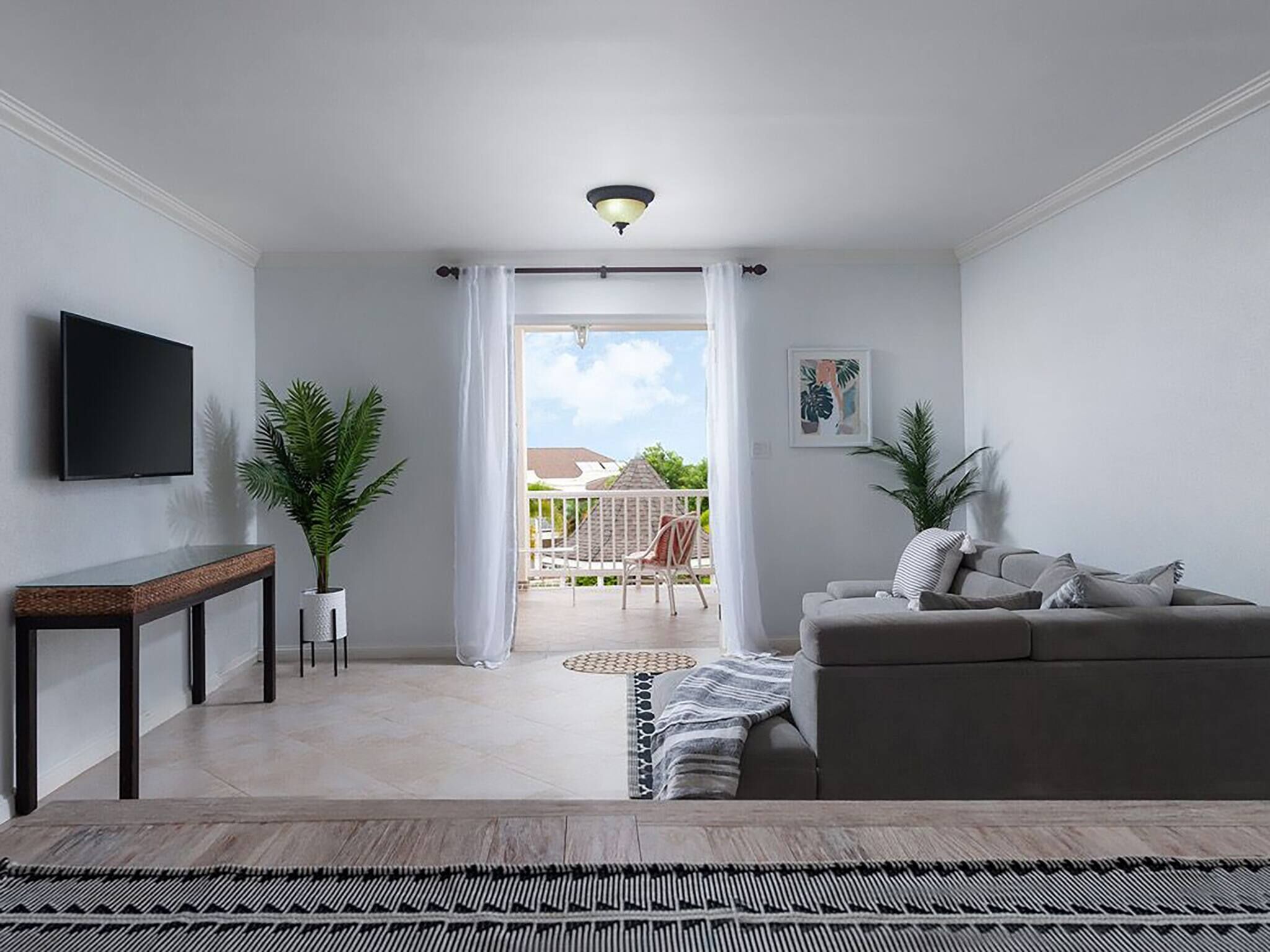A modern living room with a grey sofa, a flat-screen TV, a small table, and a potted plant.