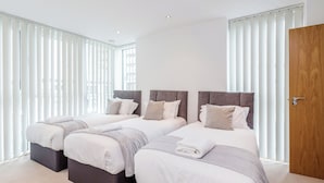 Een moderne hotelkamer met drie bedden, een houten deur en grote ramen met zonwering.