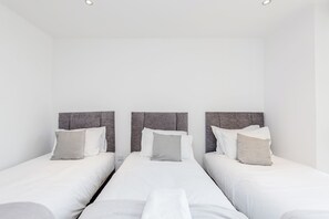 Three single beds with grey headboards and white bedding, set against a clean, minimalist backdrop.