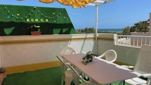 A terrace with a table and chairs, a green artificial grass floor, a white railing, and a view of the sea. - Piso Bolnuevo Playa, muy Cerca de la Playa, al Lado Todos los Servicios, (Bolnuevo)